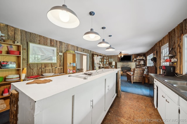 kitchen with a sink, a kitchen island, a stone fireplace, white cabinets, and hanging light fixtures