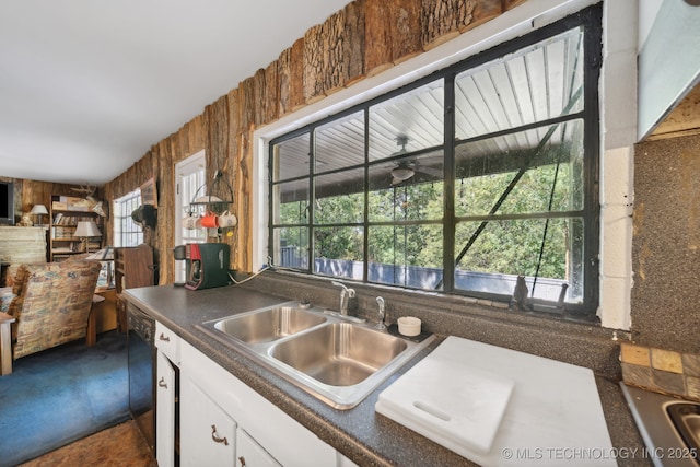 kitchen featuring a sink, dishwasher, wood walls, white cabinetry, and dark countertops