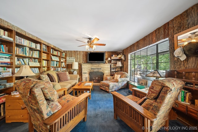 living room featuring carpet flooring, wood walls, a fireplace, and ceiling fan