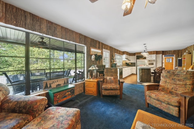 living room with wooden walls, dark colored carpet, and ceiling fan