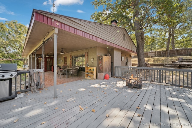 wooden terrace with grilling area, a fire pit, ceiling fan, and fence