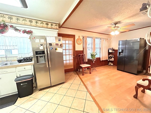 kitchen with a sink, a textured ceiling, stainless steel fridge, wainscoting, and light countertops