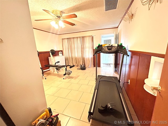 workout area with visible vents, ceiling fan, ornamental molding, wainscoting, and a textured ceiling