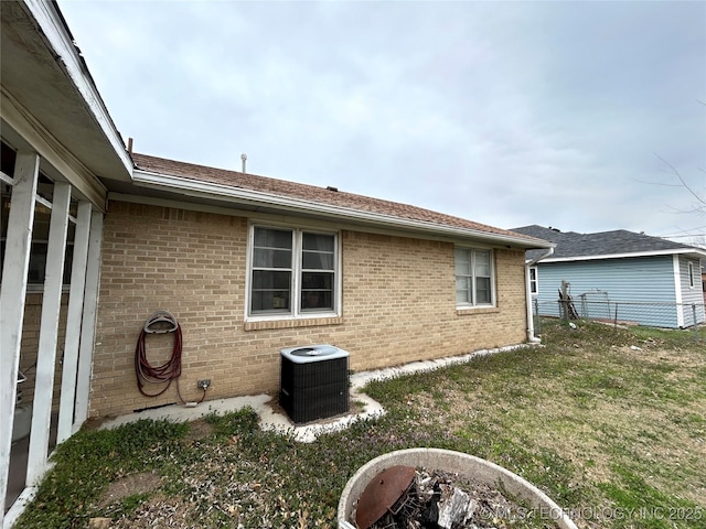 view of home's exterior featuring central air condition unit, fence, a lawn, and brick siding