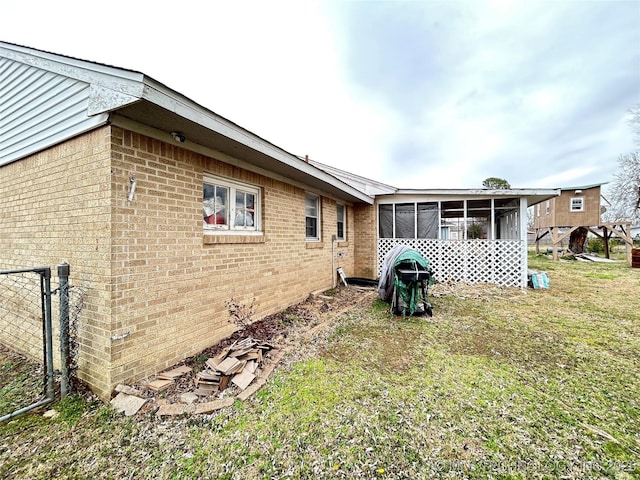 exterior space featuring a lawn, brick siding, and a sunroom