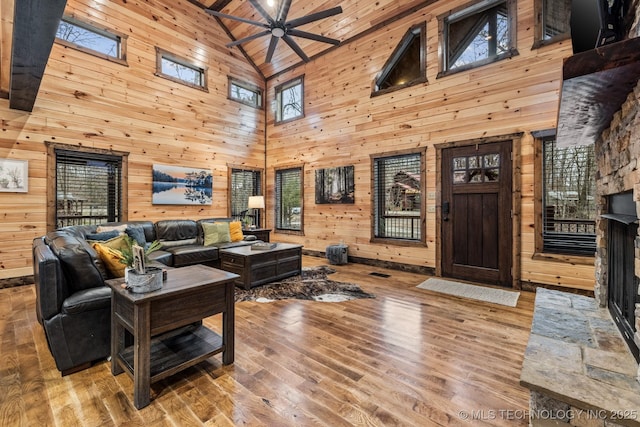 living room featuring ceiling fan, wood walls, lofted ceiling, a stone fireplace, and wood finished floors