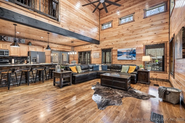 living area with wooden walls, a ceiling fan, visible vents, and light wood finished floors