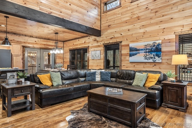 living area with light wood finished floors, a chandelier, wood walls, and a towering ceiling