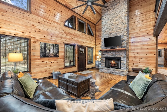 living room with a fireplace, wooden walls, wood finished floors, and a ceiling fan