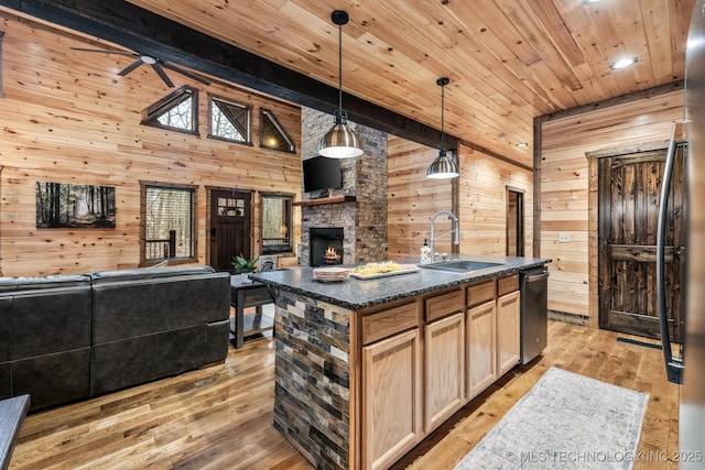 kitchen with wooden walls, light brown cabinetry, open floor plan, a fireplace, and a sink