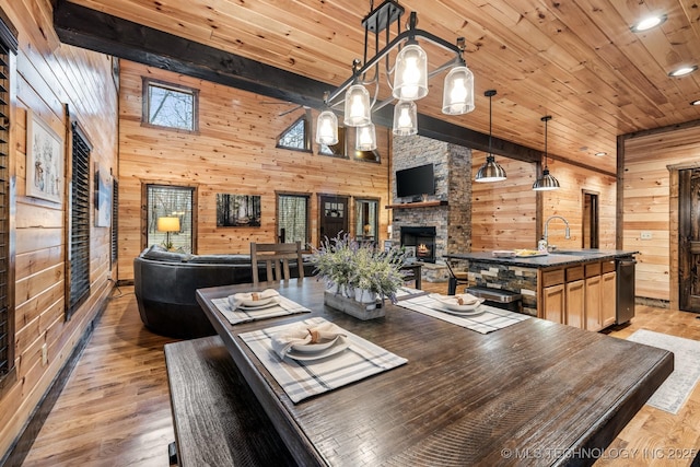 dining area with light wood finished floors, beamed ceiling, wood walls, wooden ceiling, and an outdoor stone fireplace