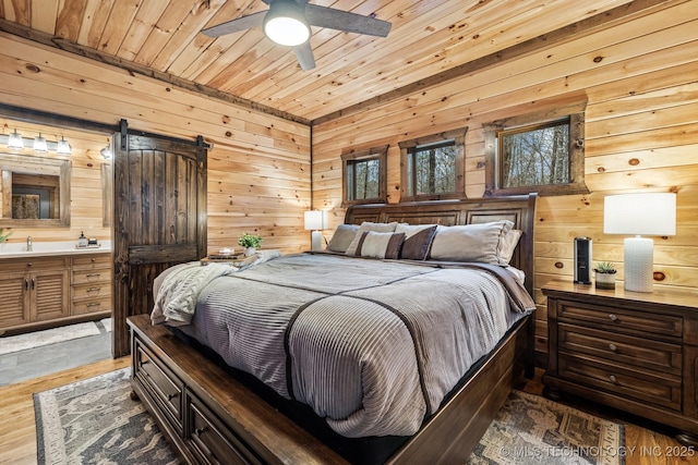 bedroom with wood walls, wooden ceiling, ensuite bathroom, and wood finished floors