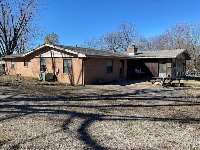 rear view of house featuring gravel driveway, brick siding, central AC, and a chimney