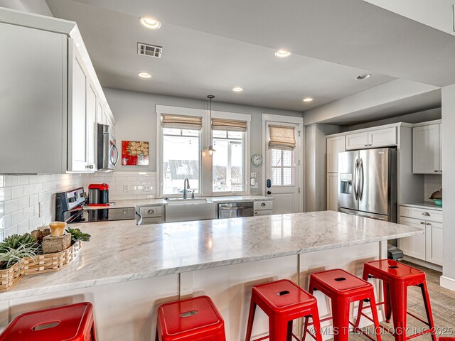 kitchen with appliances with stainless steel finishes, a sink, a peninsula, a breakfast bar area, and decorative backsplash