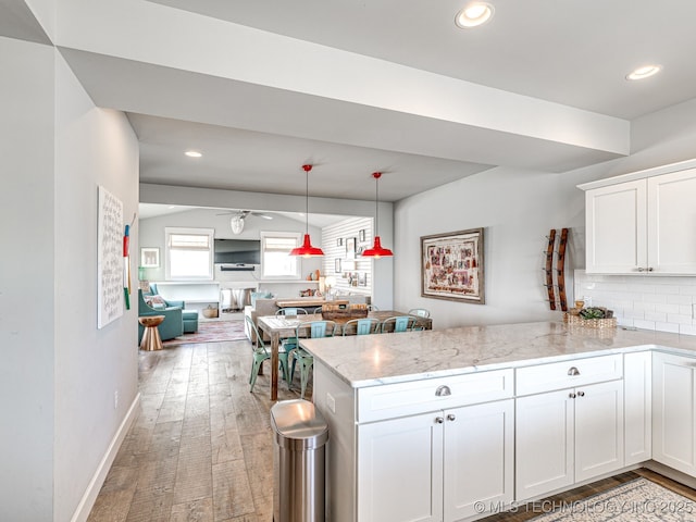 kitchen with a peninsula, white cabinets, light wood finished floors, light stone countertops, and decorative backsplash