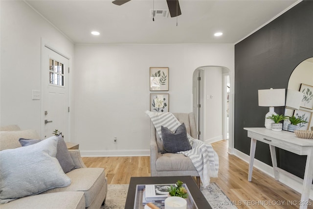 living area with baseboards, visible vents, light wood finished floors, arched walkways, and ceiling fan