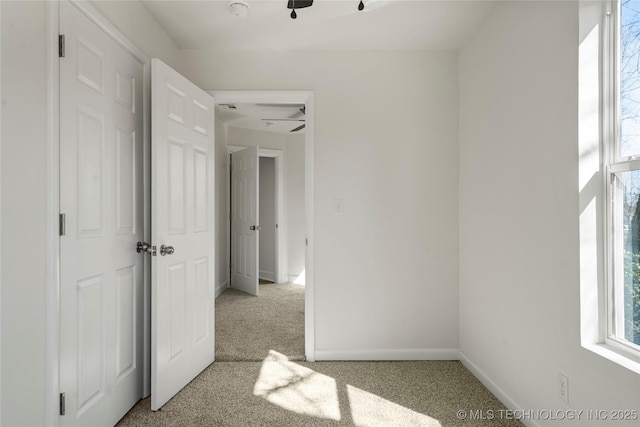 unfurnished bedroom featuring multiple windows, light colored carpet, and baseboards