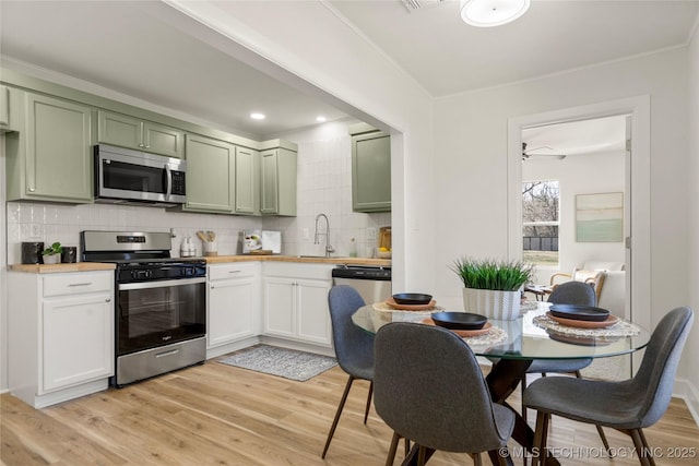 kitchen with a sink, stainless steel appliances, green cabinets, light wood-type flooring, and backsplash