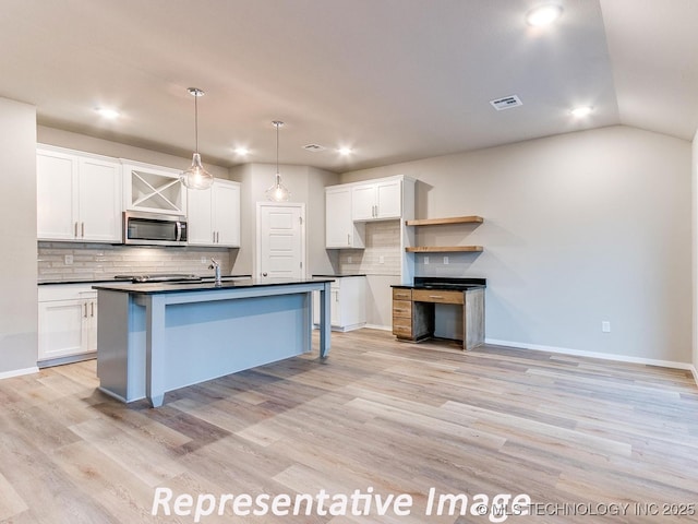 kitchen featuring visible vents, light wood-style flooring, stainless steel microwave, dark countertops, and white cabinets