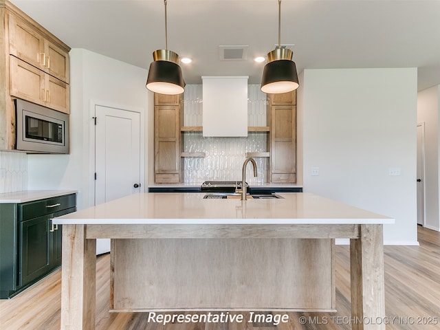 kitchen featuring open shelves, stainless steel microwave, a sink, tasteful backsplash, and light wood finished floors