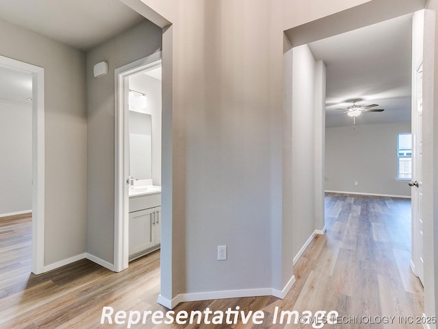 hallway with baseboards, light wood finished floors, and a sink