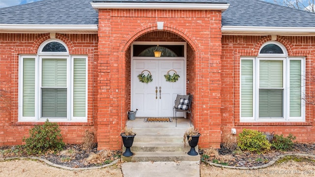 view of exterior entry featuring brick siding and a shingled roof