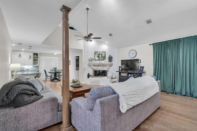 living area featuring visible vents, lofted ceiling, a fireplace, ceiling fan, and light wood-style floors