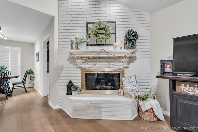 living area featuring vaulted ceiling, a fireplace, baseboards, and wood finished floors