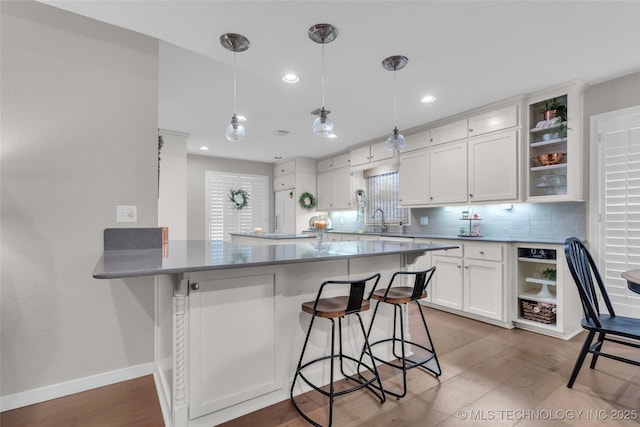 kitchen with a sink, white cabinetry, a kitchen bar, and open shelves