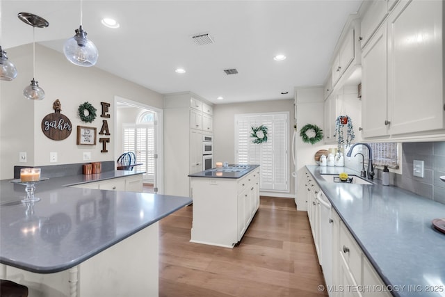 kitchen featuring light wood-style flooring, a sink, a kitchen island, dark countertops, and a peninsula