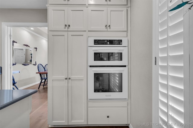 kitchen featuring baseboards, white double oven, white cabinets, and light wood finished floors