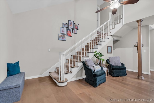 staircase with wood finished floors, baseboards, a towering ceiling, and ceiling fan