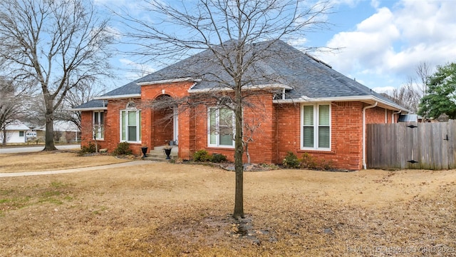 bungalow-style house featuring brick siding, a shingled roof, a front lawn, and fence