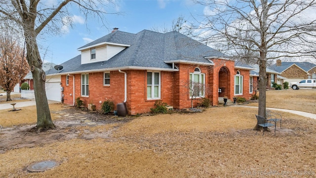 view of front of house with brick siding, an attached garage, a chimney, and roof with shingles