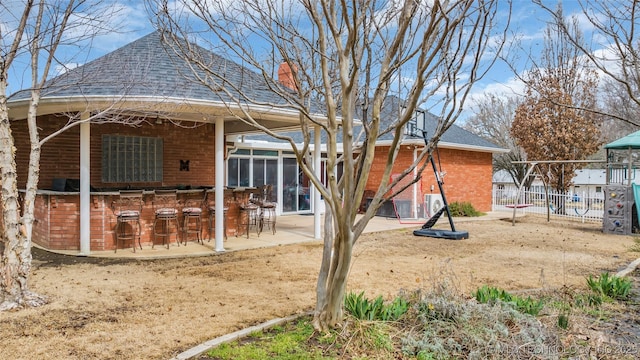 back of house featuring fence, a chimney, a shingled roof, a patio area, and outdoor dry bar