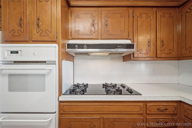 kitchen with light countertops, brown cabinets, under cabinet range hood, and black cooktop