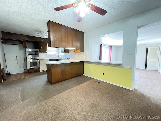 kitchen featuring light countertops, a peninsula, stainless steel appliances, a textured ceiling, and a ceiling fan