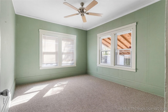 carpeted spare room featuring ceiling fan, a decorative wall, and ornamental molding