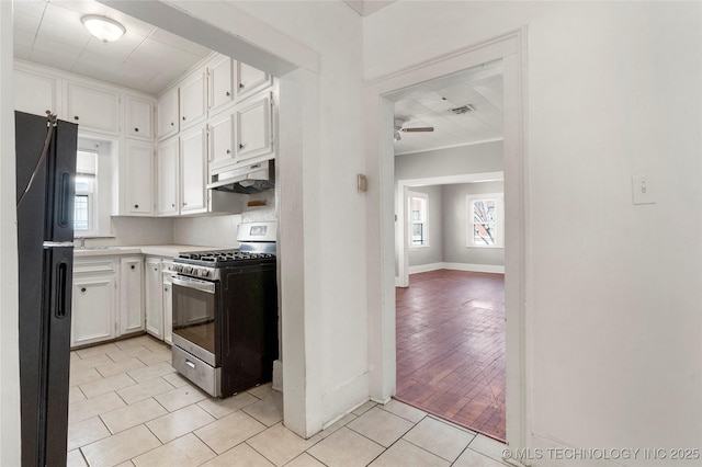 kitchen with light tile patterned floors, a ceiling fan, stainless steel gas range, freestanding refrigerator, and under cabinet range hood