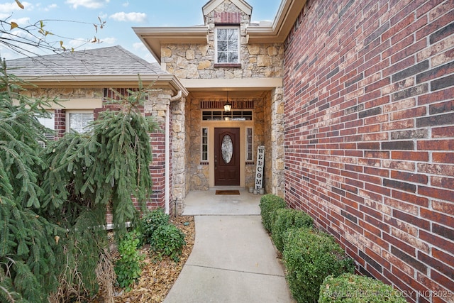 doorway to property with stone siding and a shingled roof