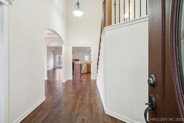 hallway with a high ceiling, dark wood-style floors, arched walkways, and baseboards