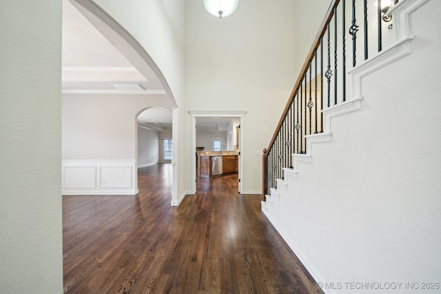 entrance foyer featuring stairway, arched walkways, dark wood-style flooring, crown molding, and a decorative wall