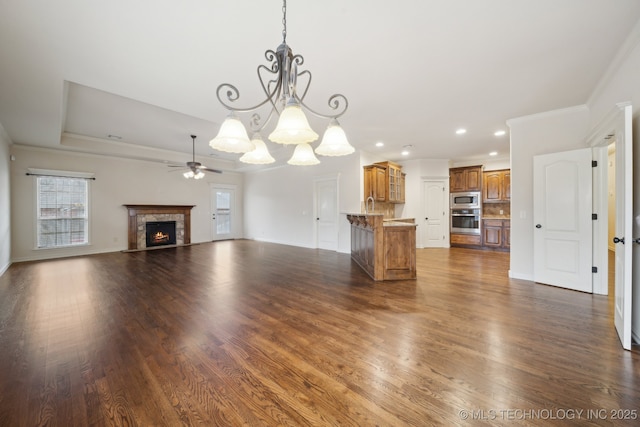 unfurnished living room featuring a lit fireplace, ornamental molding, recessed lighting, ceiling fan with notable chandelier, and dark wood-style floors