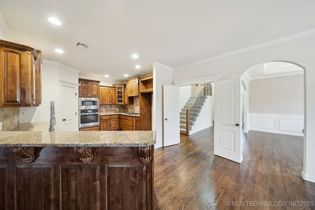 kitchen featuring dark wood-style floors, a peninsula, stainless steel appliances, and crown molding