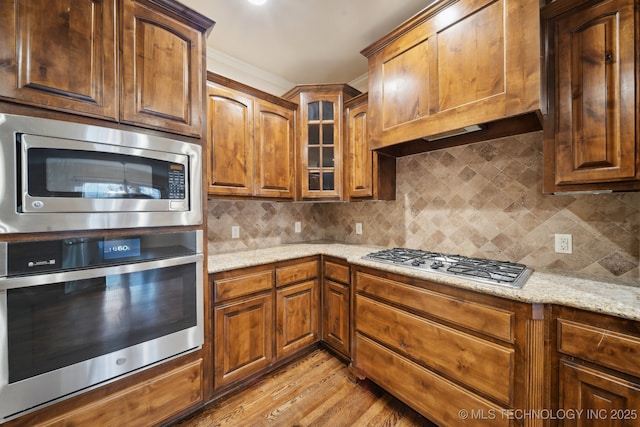 kitchen with premium range hood, backsplash, stainless steel appliances, light wood finished floors, and light stone countertops