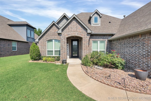 view of front of home featuring a front lawn, brick siding, and roof with shingles