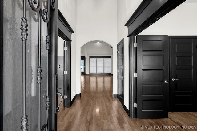 hall with arched walkways, a towering ceiling, baseboards, and wood finished floors