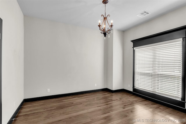 empty room featuring baseboards, wood finished floors, visible vents, and a chandelier