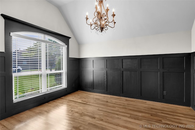 unfurnished dining area with a wealth of natural light, light wood finished floors, a decorative wall, a chandelier, and vaulted ceiling