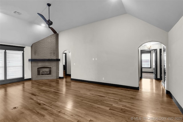 unfurnished living room featuring arched walkways, a fireplace, wood finished floors, and a ceiling fan